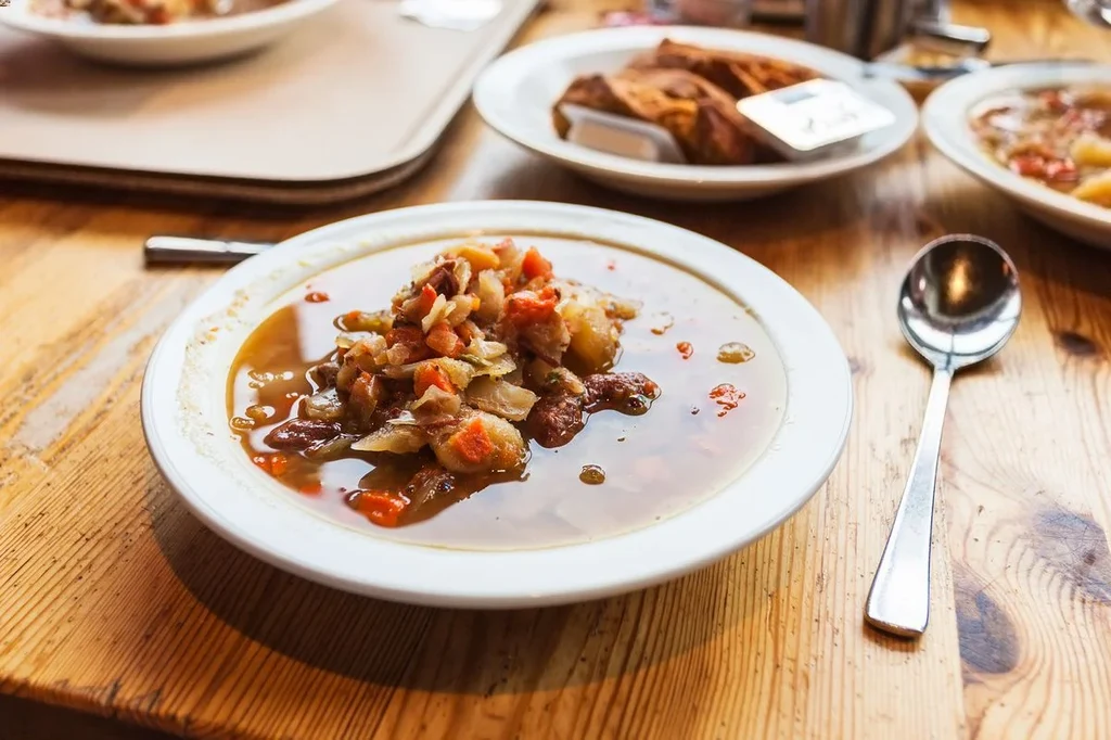 A close-up of a bowl of traditional Icelandic lamb soup served on a wooden table. The soup is filled with chunks of tender lamb, root vegetables, and a flavorful broth, accompanied by a spoon on the side.