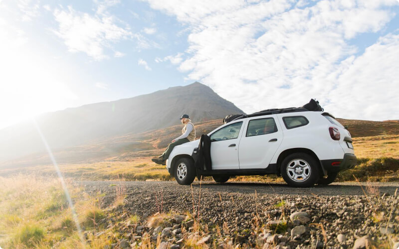 A traveler leans against a white car, parked on a scenic road in Iceland.