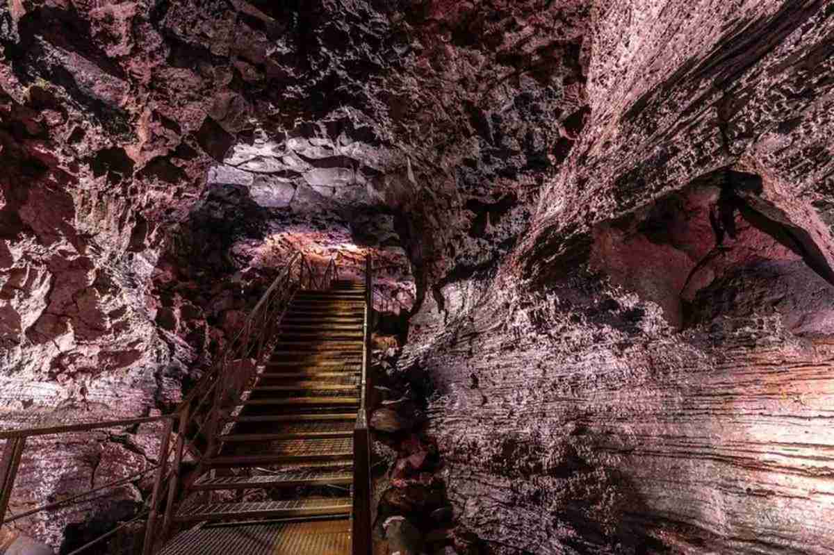 Inside Raufarholshellir lava tunnel, featuring a dramatic stairway surrounded by layered volcanic rock formations and skylit cave walls.