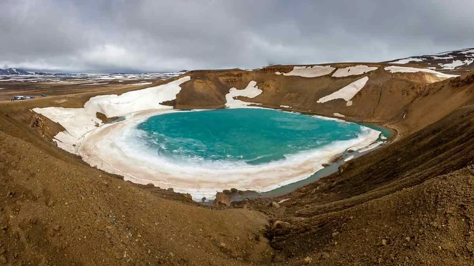 Kerid volcanic crater lake with vibrant turquoise water surrounded by contrasting red and black volcanic rocks, partially covered with snow.