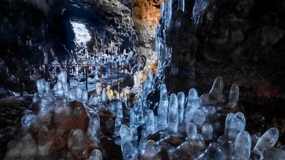 Vast lava tunnel of Raufarholshellir featuring stunning ice stalagmites, colorful rock formations, and a unique skylit volcanic cave landscape.