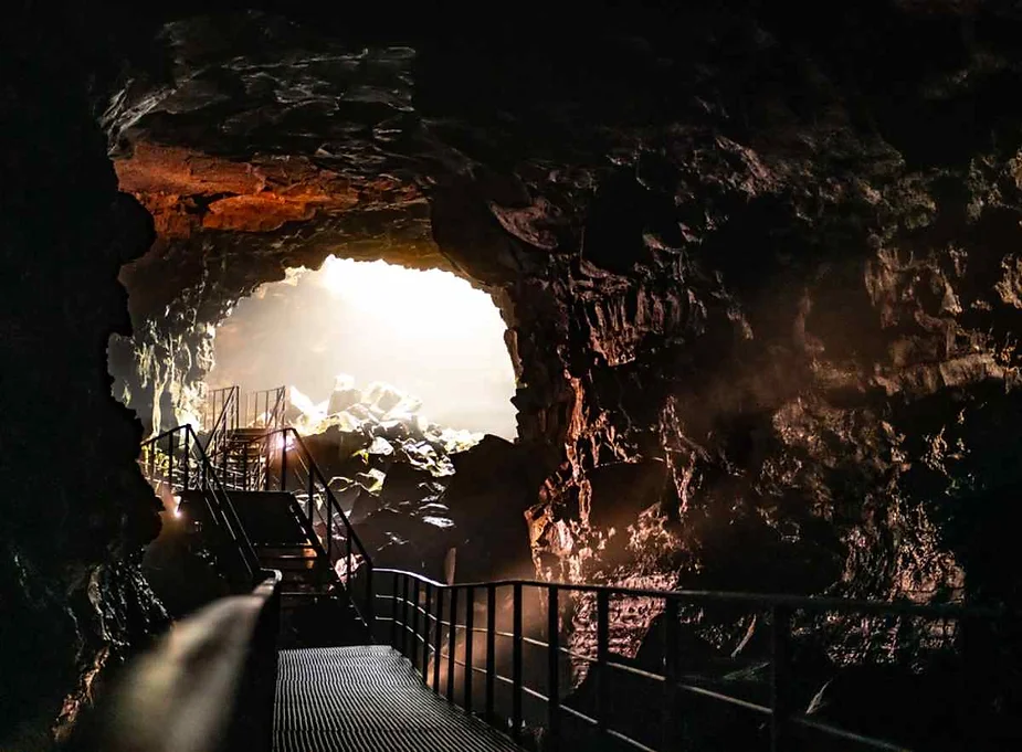 Sunlight streaming through the skylight of Raufarholshellir lava tunnel, illuminating the rugged volcanic rock formations and stairways.