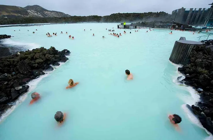 People bathing in the milky blue waters of the Blue Lagoon, a famous geothermal spa in Iceland, surrounded by rocky terrain and modern facilities.