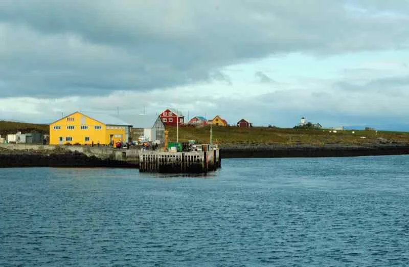 Colorful houses and a small dock at a coastal village near Ísafjörður, Iceland, under a cloudy sky with scenic views of the surrounding waters.