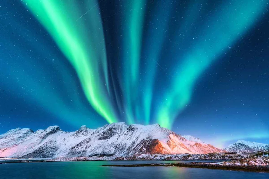 Stunning Northern Lights over snow-capped mountains in Iceland, with green auroras lighting up the clear night sky above Ísafjörður.