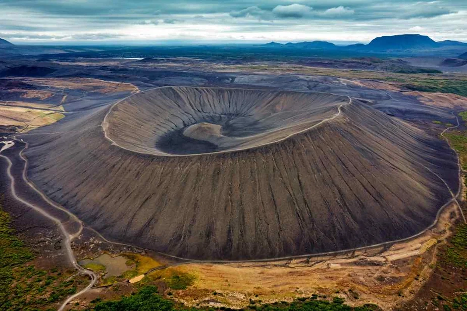 Stunning aerial view of Hverfjall crater in Iceland, a massive volcanic feature surrounded by rugged lava fields and lush greenery.