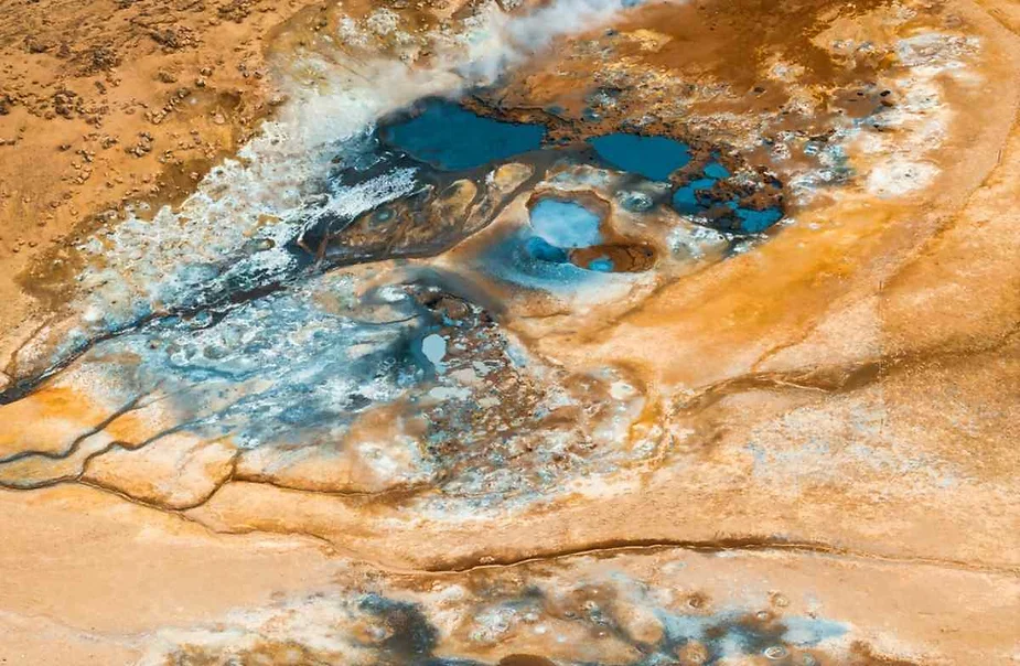 Colorful mud pools at Hverir, Iceland, showcasing boiling hot sulfuric pools surrounded by vibrant mineral deposits and rugged terrain.