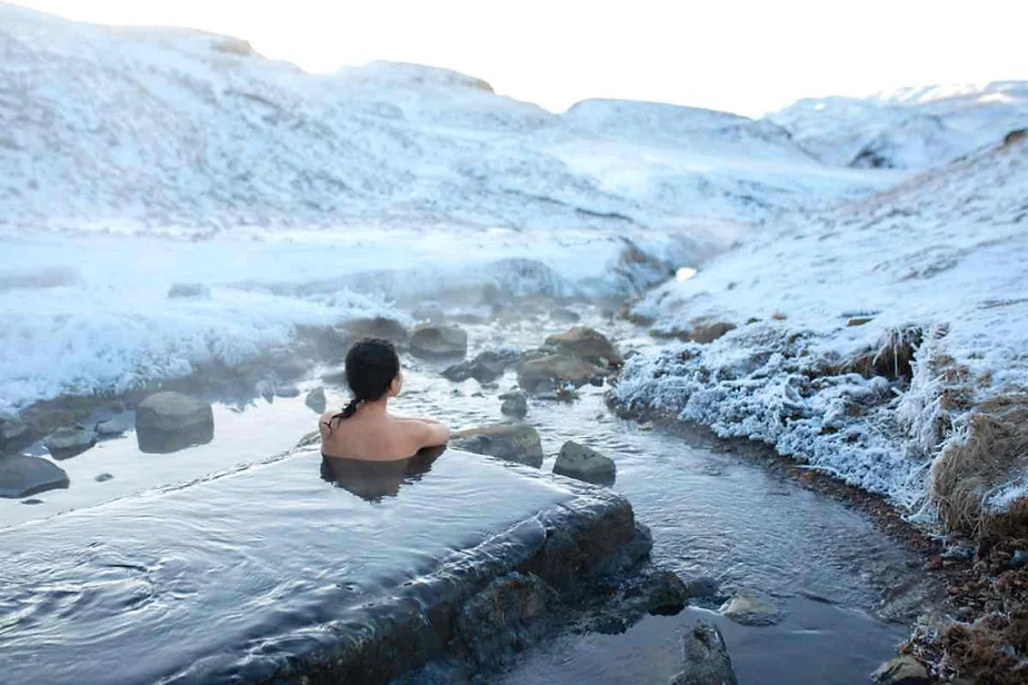 Relaxing in a natural geothermal pool surrounded by snowy landscapes in Iceland, offering a serene and rejuvenating experience.