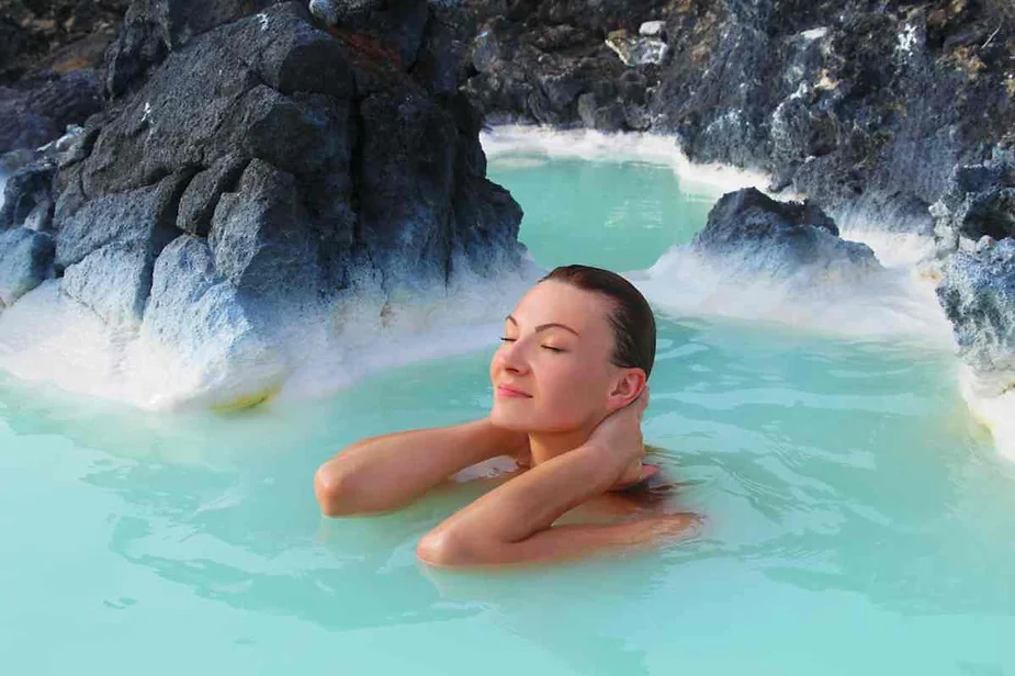 Relaxing in a natural hot spring in Iceland, surrounded by black volcanic rocks and vibrant turquoise geothermal waters.