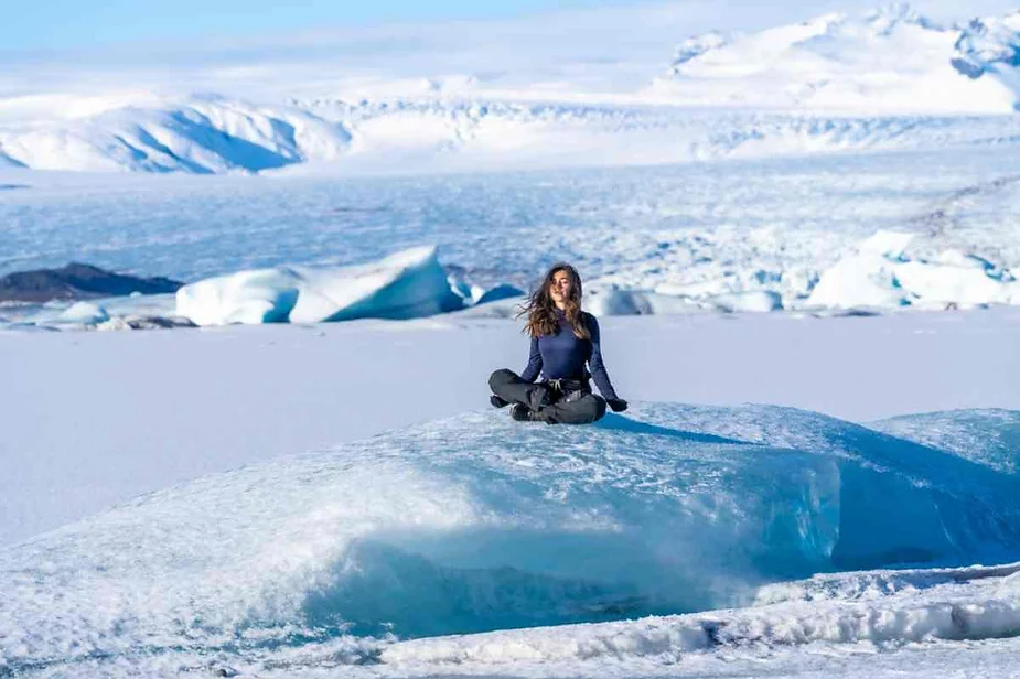 Traveler meditating on an ice block at Vatnajökull Glacier, Iceland, surrounded by vast icy landscapes and snowy mountain peaks.