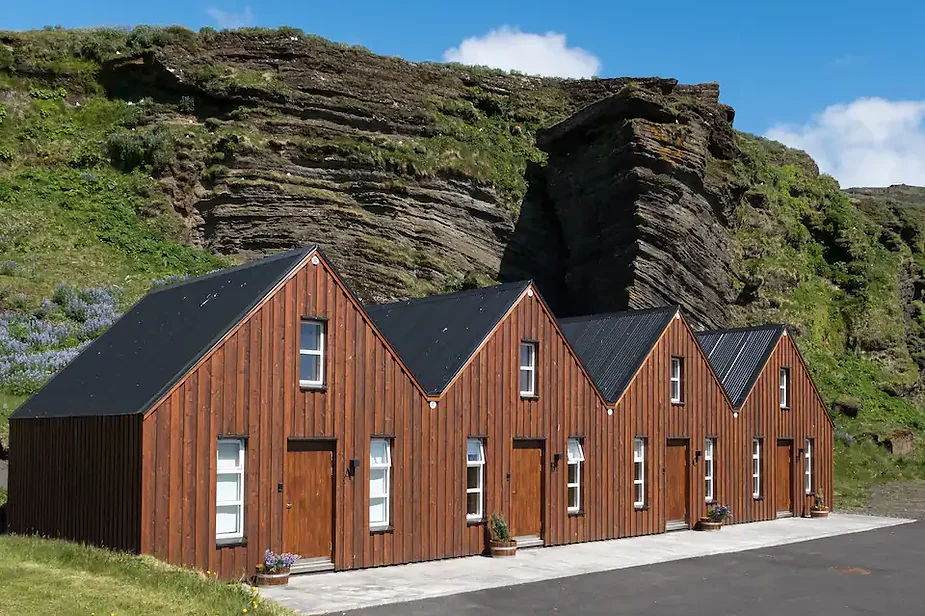 Modern wooden cabin in Vik, Iceland, set against dramatic cliffs and surrounded by lush greenery, offering a cozy retreat near Reynisfjara Beach.