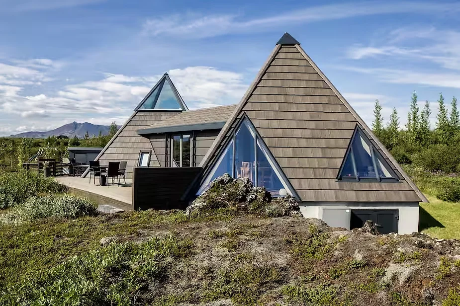 Modern triangular cottage near Geysir, Iceland, surrounded by moss-covered lava fields, offering geothermal heating and stunning Golden Circle views.