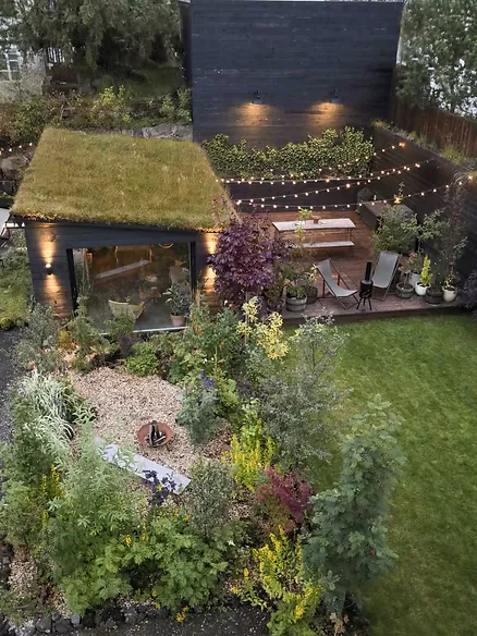 Luxury designer cottage near Reykjavik, Iceland, featuring a lush garden, greenhouse, and cozy outdoor dining space with string lights.