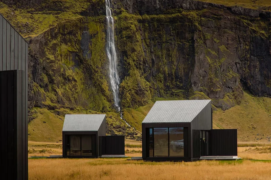 Modern black cottages near Seljalandsfoss waterfall in Iceland, set against lush green cliffs, offering a serene and picturesque retreat.