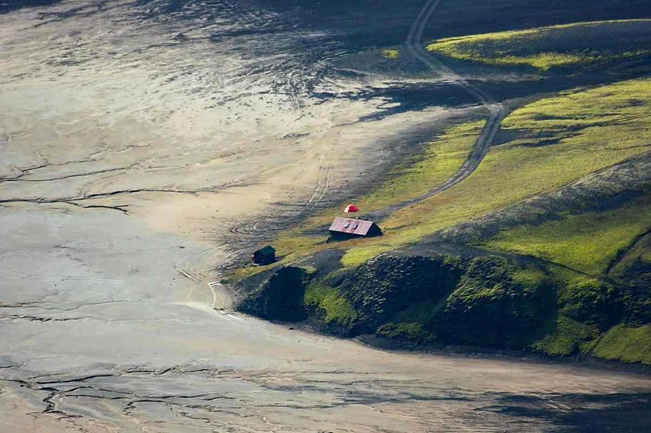 Remote campsite near Langisjór Lake in Iceland, featuring a small red-roofed hut surrounded by lush green hills and volcanic plains.