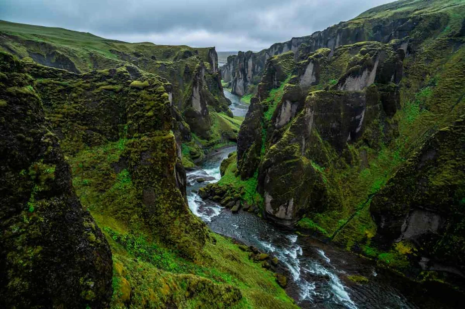 Fjaðrárgljúfur Canyon in Iceland, featuring dramatic winding cliffs covered in lush green moss with a glacial river flowing through the valley.