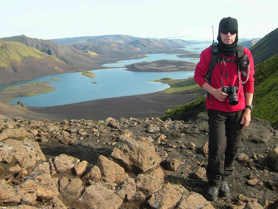 Traveler at Langisjór Lake in Iceland, surrounded by volcanic terrain and pristine blue waters, with hiking gear and a camera.