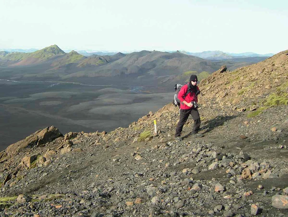 Adventurous hiker scaling a rocky trail on the Sveinstindur Trail in Iceland, surrounded by breathtaking volcanic landscapes and panoramic views.