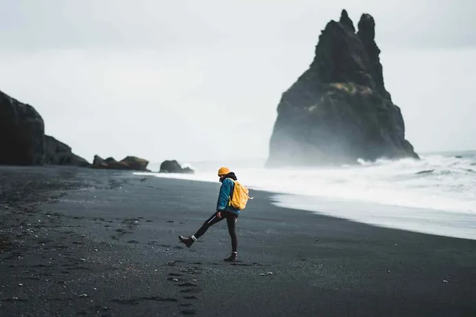 Visitor with a yellow backpack at Reyknisfjara beach in Iceland