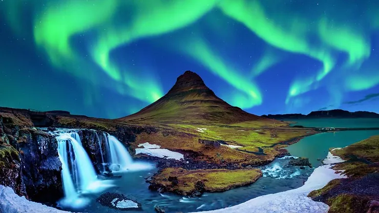 Stunning view of the Northern Lights dancing over Kirkjufell Mountain with a waterfall and vibrant landscape in Iceland.