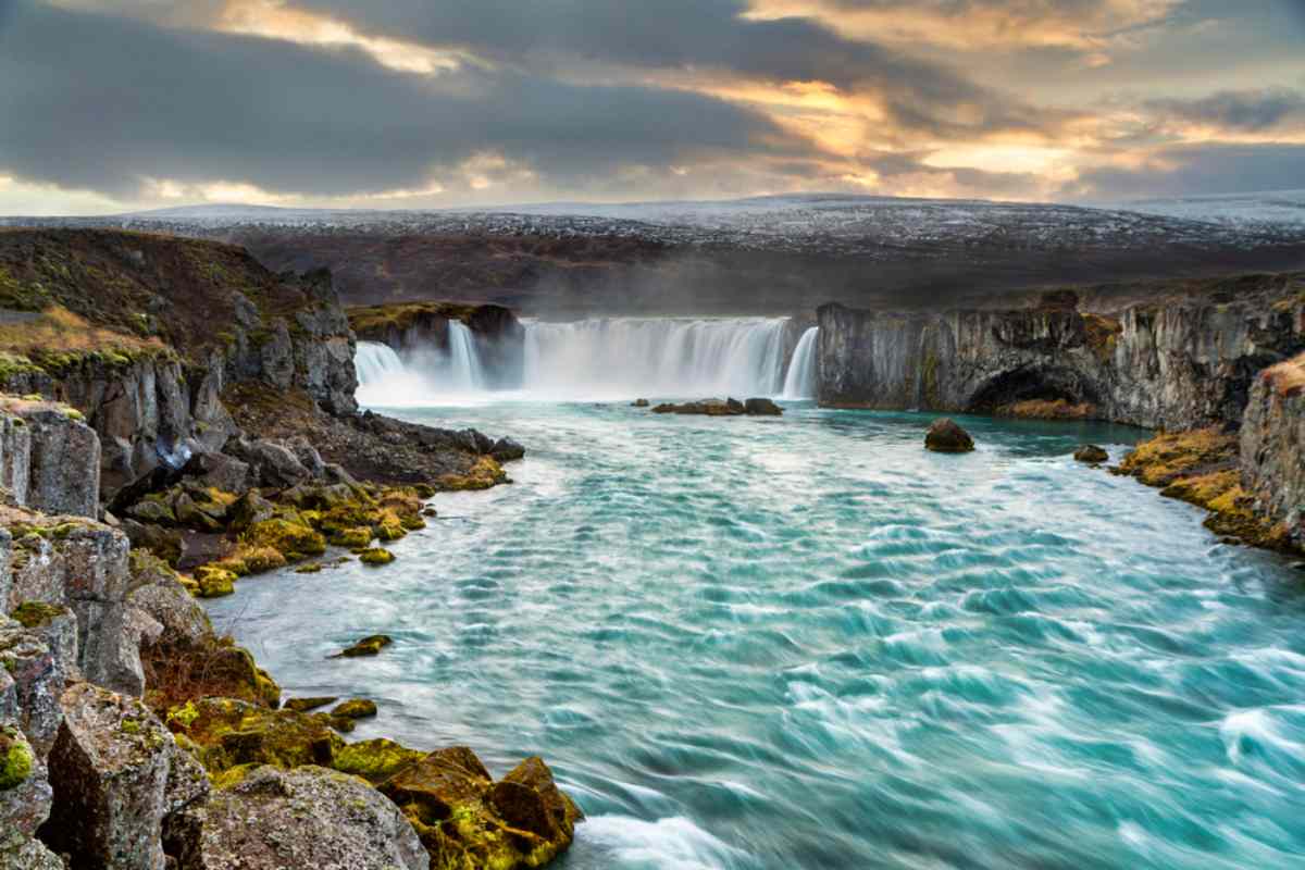 Beautiful waterfall with turquoise waters and snowed mountains on the back