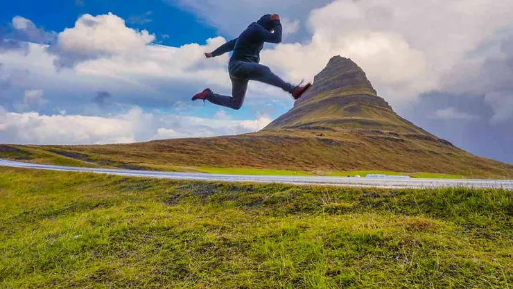 Person jumping with joy in front of the majestic Kirkjufell mountain, showcasing a sense of adventure and freedom during a hike.