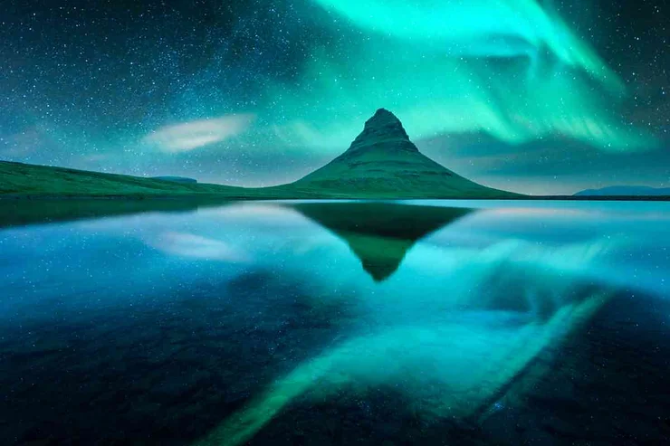 Breathtaking display of the Northern Lights dancing over Kirkjufell mountain, perfectly reflected in the calm waters below.