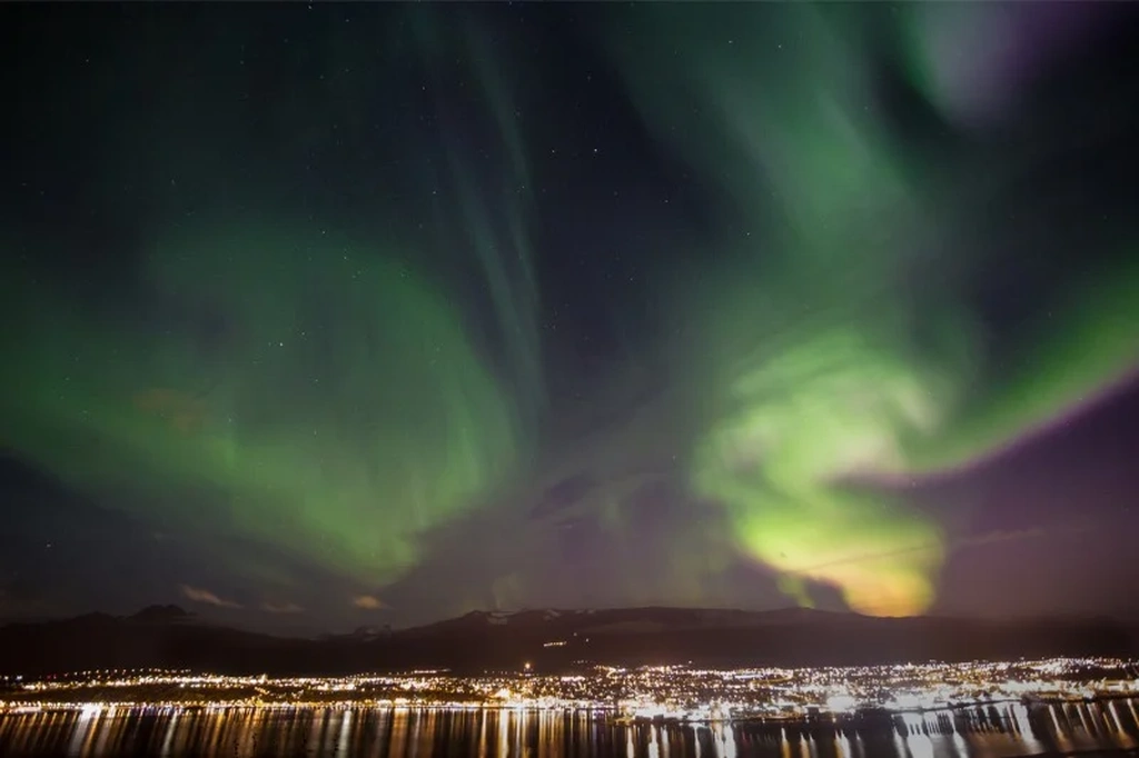 The Northern Lights illuminate the night sky over Akureyri, Iceland, with vivid green and purple hues dancing across the sky.