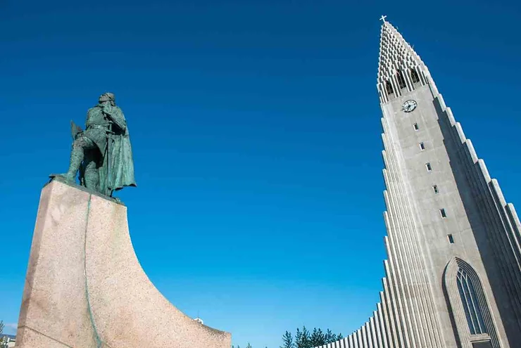 A statue in front of the iconic Hallgrimskirkja Cathedral in Reykjavik, Iceland, against a clear blue sky.