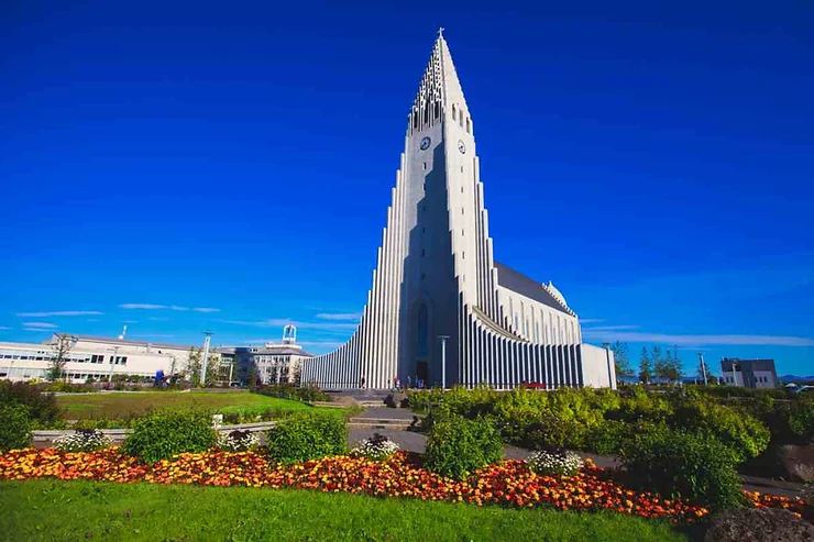 Hallgrimskirkja Cathedral in Reykjavik, Iceland, with vibrant flower beds in the foreground and a clear blue sky above.