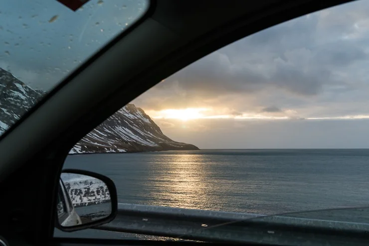 View of the ocean and mountains through a car window while driving in Iceland at sunset.