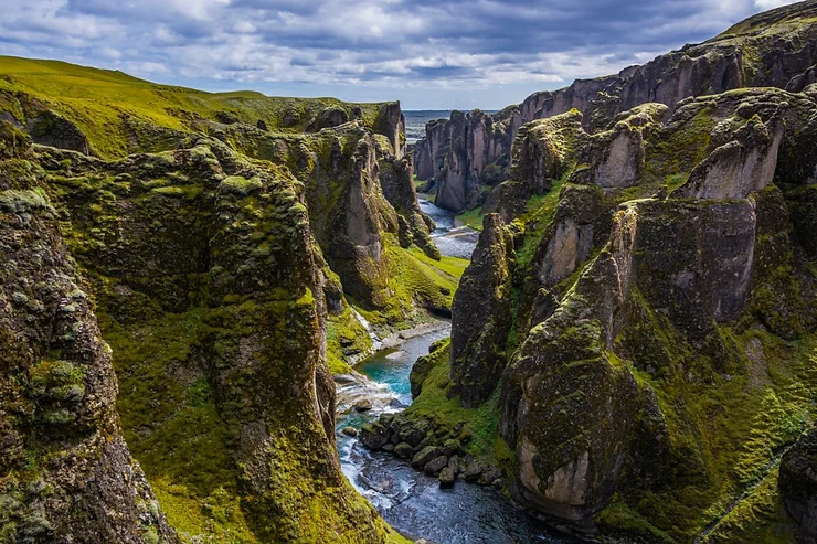 Aerial view of Fjadrargljufur Canyon in Iceland, showcasing steep moss-covered cliffs and a winding river flowing through the valley.