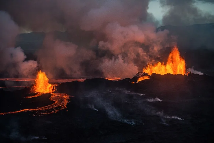 Erupting lava flow at Holuhraun with glowing orange lava and billowing smoke during an eruption in Iceland.