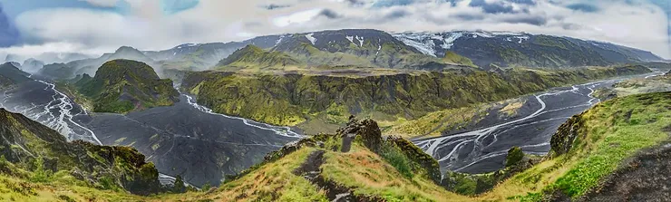 A panoramic view of Vesturdalur Valley with winding rivers, lush green hills, and distant snow-capped mountains in Iceland.