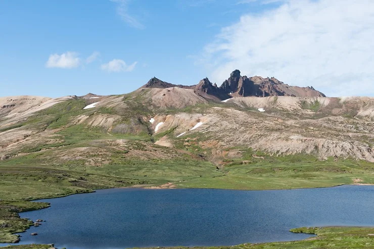 Scenic view of the Viknaslodir hiking area with a serene lake in the foreground and rugged mountains in the background under a clear blue sky in Iceland.