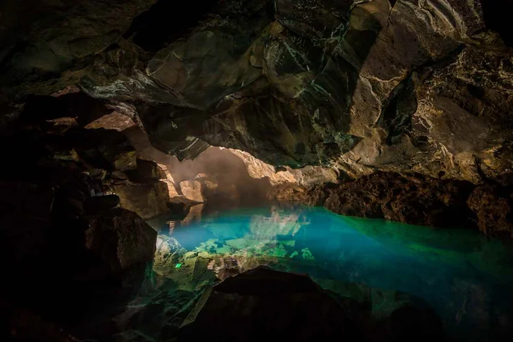 Grjótagjá cave with turquoise water illuminated by soft light, surrounded by rugged rocky formations.