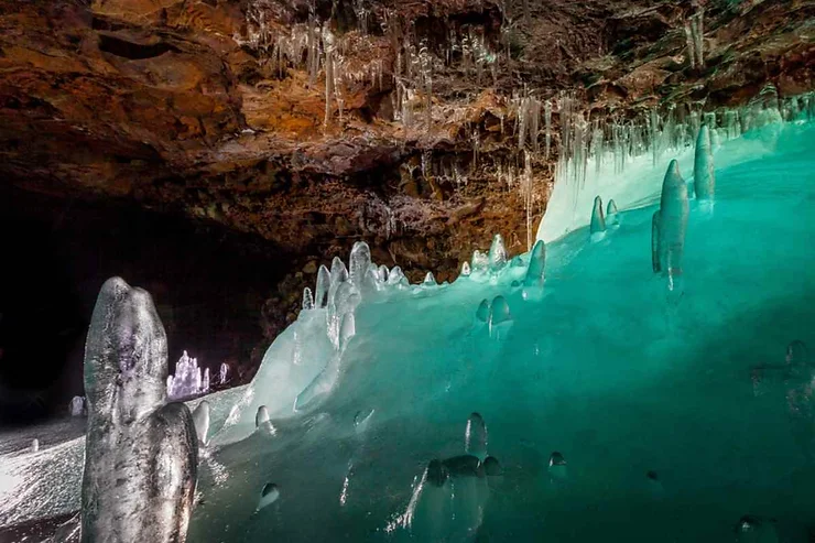 Lava Cave in Iceland with striking ice formations, glistening under a rocky ceiling with a greenish hue.