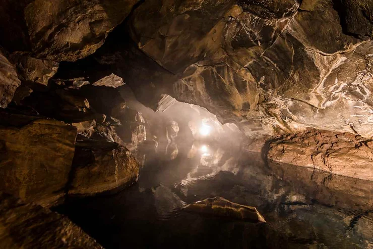 Lofthellir cave with mystical lighting reflecting off the rocky walls and water surface inside the cave.