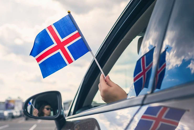 A person holding an Icelandic flag out of a car window, symbolizing driving in Iceland with the correct documentation.