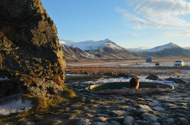 A person relaxing in a hot spring surrounded by snowy mountains and a clear sky in Iceland, representing typical weather in May.