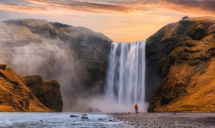 A serene view of Skógafoss waterfall in Iceland, surrounded by autumn foliage and mist, illustrating the typical weather in September.