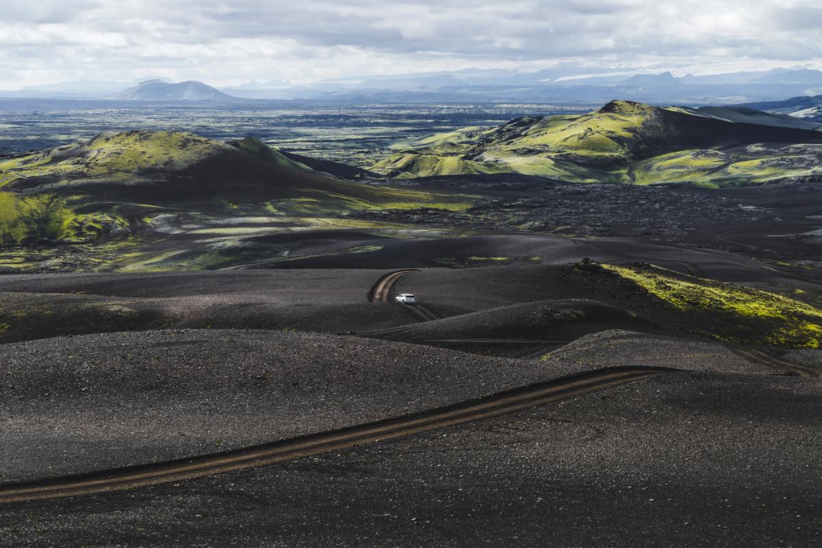 Road in the highlands of Iceland covered in black volcanic ash and a vehicle driving through it