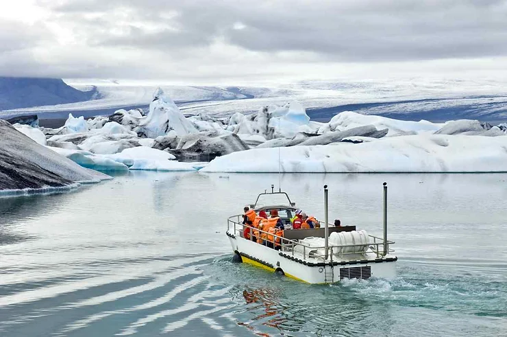 A boat carrying tourists navigates through the icebergs in Jökulsárlón Glacier Lagoon, Iceland, under a cloudy October sky.