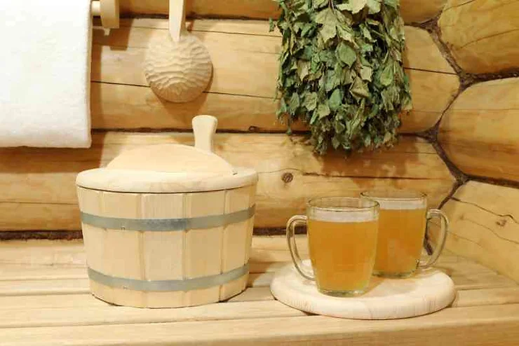 Two glasses of beer on a wooden coaster inside a cozy beer spa in Iceland, with a traditional sauna bucket and dried herbs hanging on the wooden wall.