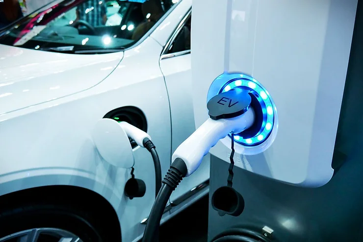 Close-up image of an electric vehicle (EV) charging at a station, highlighting the EV plug connected to the car with a blue illuminated charging port.