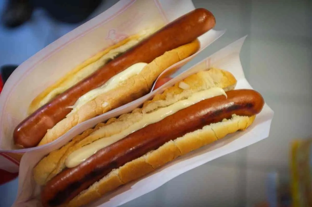 A close-up of two Icelandic hot dogs served in soft buns, generously topped with a creamy white sauce. The sausages are perfectly grilled, showcasing a rich, juicy texture. These hot dogs are a popular street food in Iceland, often enjoyed with a variety of toppings including crispy onions and a mix of sauces. The simple yet delicious meal highlights Iceland's unique twist on the classic hot dog.