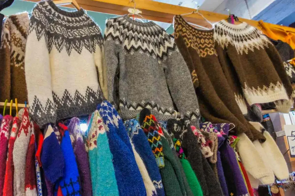 A vibrant display of traditional Icelandic sweaters, known as lopapeysa, hanging in a souvenir shop. These woolen sweaters feature distinctive geometric patterns in shades of white, gray, brown, and colorful hues, highlighting the intricate knitting craftsmanship. The lopapeysa is an iconic Icelandic garment, cherished for its warmth and unique style, making it a popular souvenir choice for visitors to Iceland.