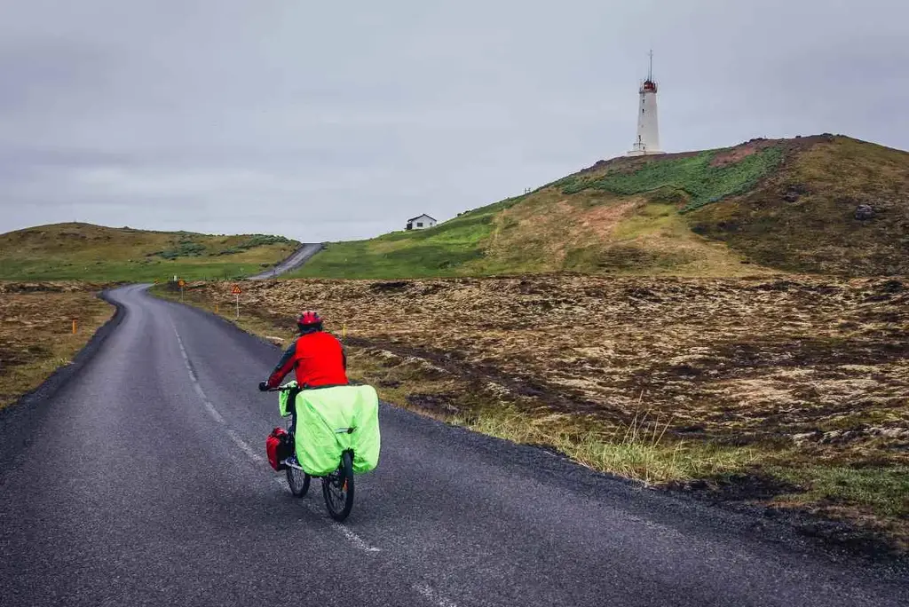 A cyclist rides towards a lighthouse on Iceland's South Coast Lighthouse Trail.