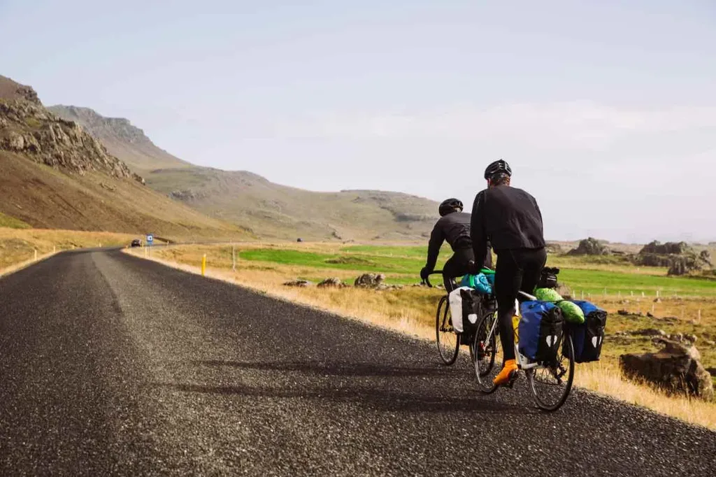 Two cyclists ride along Iceland's Ring Road, carrying panniers loaded with gear.