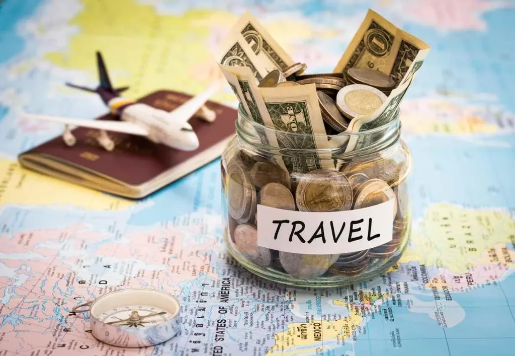 A glass jar labeled 'travel' filled with various currencies including coins and bills, symbolizing saving for expenses. The jar sits on a world map, suggesting planning a trip, with a nearby toy airplane, passport, and compass emphasizing preparation and exploration. The image conveys a concept of budgeting for an upcoming adventure, focusing on excitement and exploring new destinations.